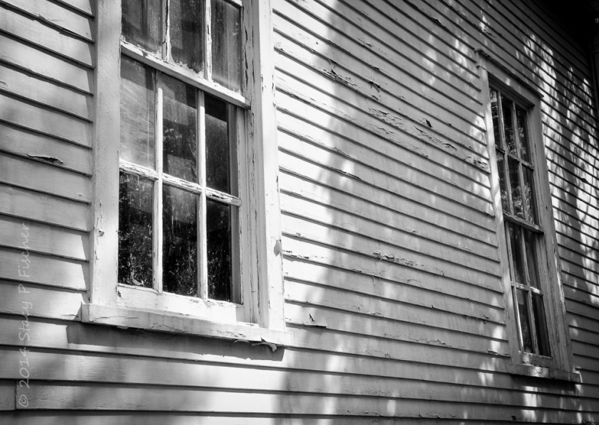 Side view of wooden building, paint peeling from boards and around two paned windows.